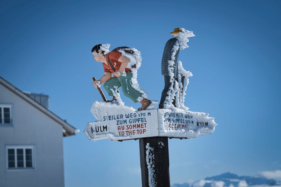 Detailed view of a snow-covered hiking sign pointing to the summit on a clear winter day.