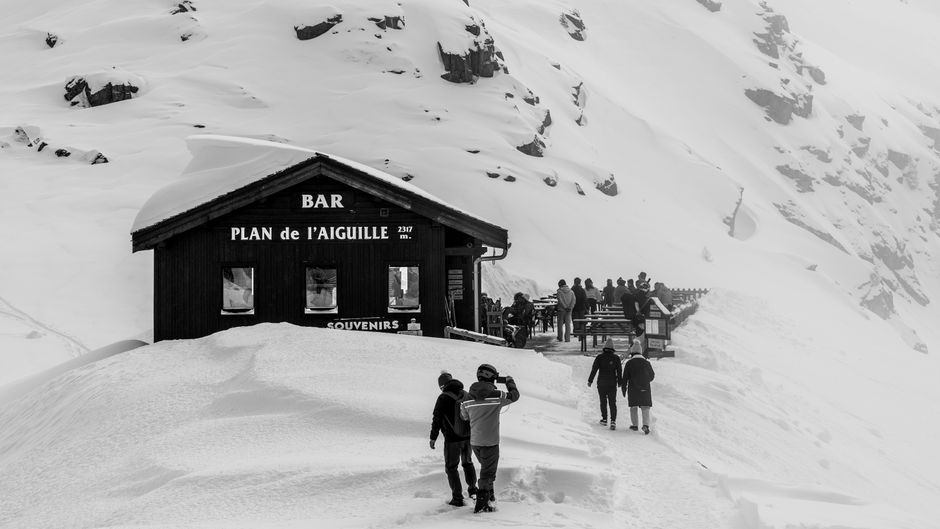 A snowy winter scene at Plan de l'Aiguille in Chamonix, featuring a mountain bar and bundled-up visitors.