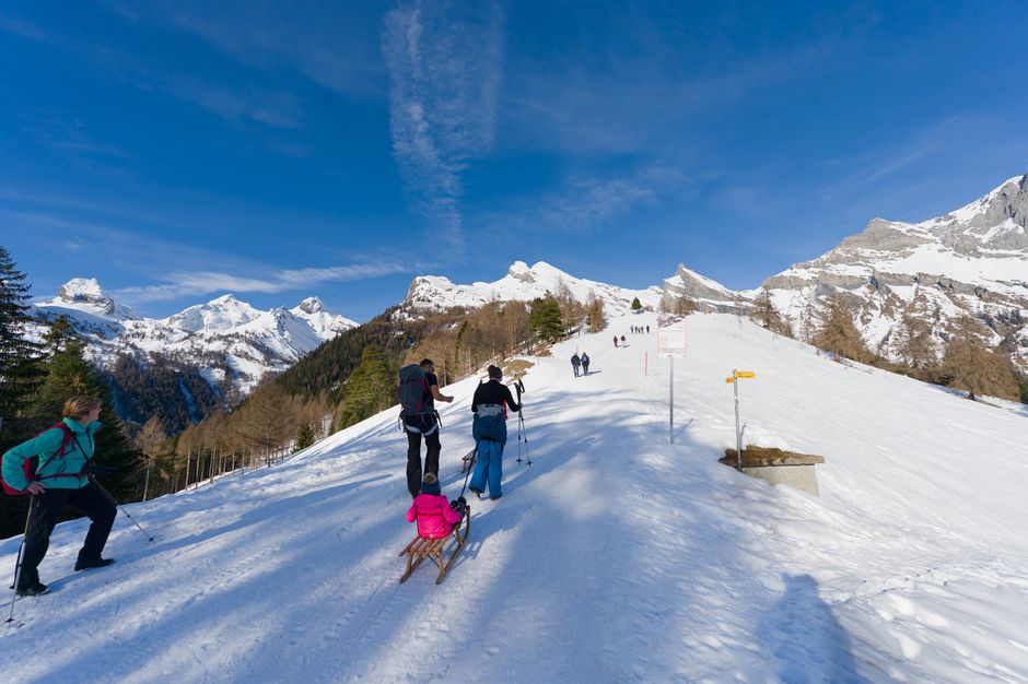 Group of hikers ascending a snowy mountain trail in the Swiss Alps under a clear blue sky.
