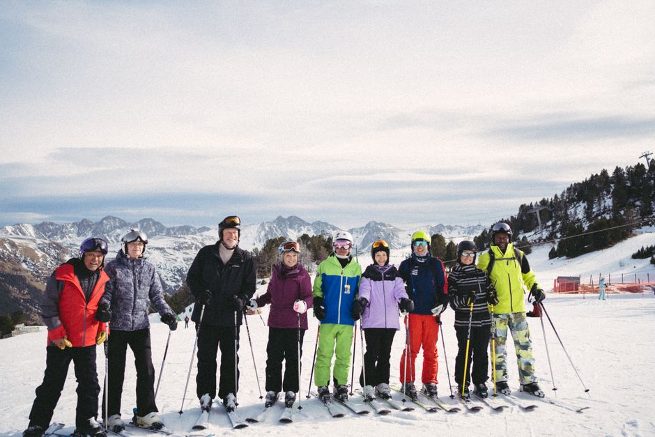 A diverse group of skiers posing on a ski slope against a snowy mountain backdrop.