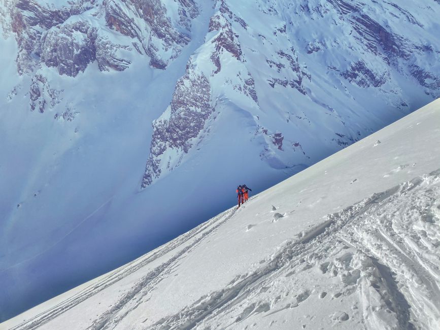 Unrecognizable skiers skiing on snowy vast valley towards rocky severe mountain range on sunny winter day