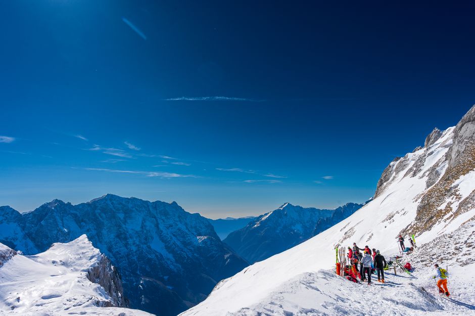 A group of skiers on a sunlit snowy mountain with a clear blue sky.